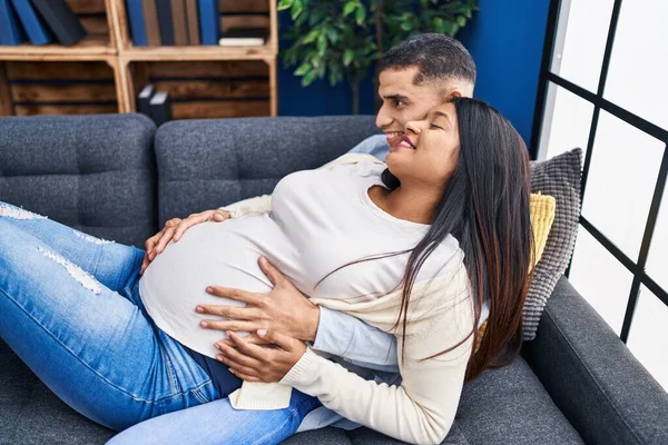 年轻的拉丁夫妇期待着宝宝摸着肚子躺在家里的沙发上 — 图库照片