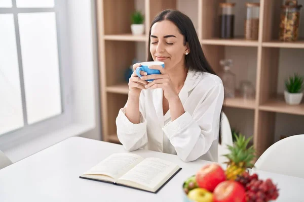 Young Hispanic Woman Reading Book Drinking Coffee Home — Foto de Stock