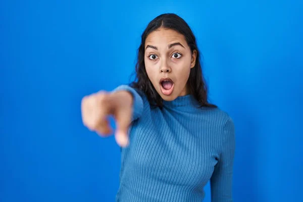 若いブラジル人女性の青の孤立した背景の上に指を前に 口を開いて驚いて表現 何かを前に驚いて指して立って — ストック写真