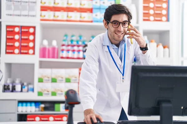 年轻的恐慌男子药剂师在药店用电脑用智能手机交谈 — 图库照片