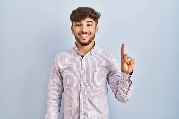 自信と幸せを笑顔ながら 青の背景が表示され 指の番号1を指摘しながら 髭を生やしたアラブ人の男 — ストック写真