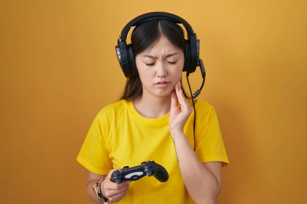 中国年轻女子手牵着控制器玩电子游戏 手摸嘴时 由于牙痛或牙病而表现出疼痛的表情 牙医概念 — 图库照片