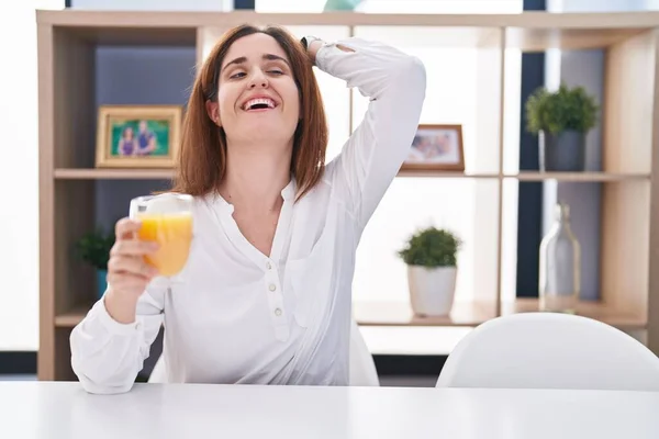 ブルネット女性飲むガラスのオレンジジュース笑顔自信を持ってタッチ髪で手をジェスチャー ポーズ魅力的かつファッショナブルな — ストック写真