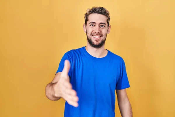 stock image Hispanic man with beard standing over yellow background smiling friendly offering handshake as greeting and welcoming. successful business. 