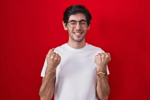 Молодой Латиноамериканец Стоящий Красном Фоне Взволнованный Успехом Поднятыми Руками Закрытыми — стоковое фото