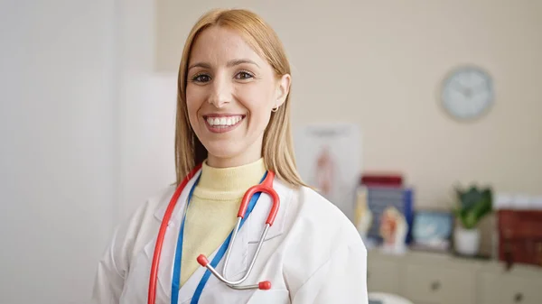 Νεαρή Ξανθιά Γυναίκα Γιατρός Χαμογελά Αυτοπεποίθηση Στέκεται Στην Κλινική — Φωτογραφία Αρχείου