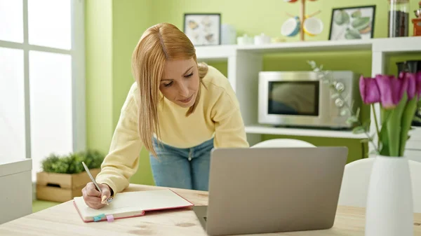 年轻的金发女人在家里的笔记本上用笔记本电脑写字 — 图库照片