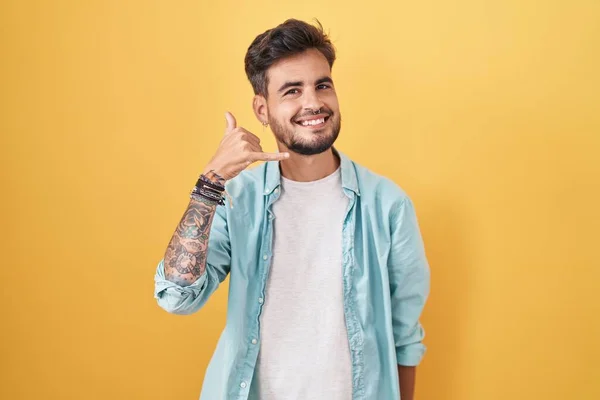 Sarı Arka Planda Dikilen Dövmeli Genç Spanyol Adam Telefonla Parmaklarıyla — Stok fotoğraf