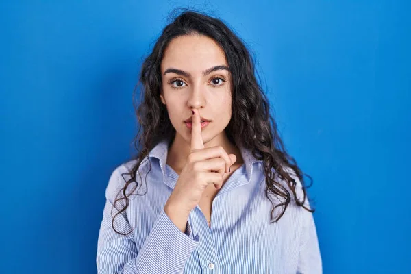 年轻的黑发女人站在蓝色的背景上要求安静 手指放在嘴唇上 沉默和秘密概念 — 图库照片