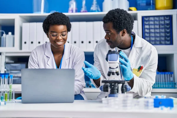 アフリカ系アメリカ人の男性と女性の科学者が実験室でノートパソコンと顕微鏡を使って — ストック写真