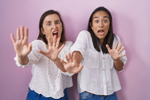 Hispanic mother and daughter together afraid and terrified with fear expression stop gesture with hands, shouting in shock. panic concept.