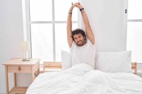 Young Hispanic Man Waking Stretching Arms Bedroom – stockfoto