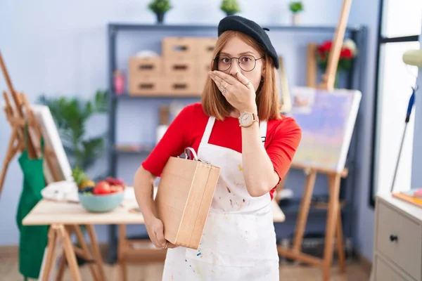 Young Redhead Woman Art Studio Holding Art Case Shocked Covering — Stock Photo, Image