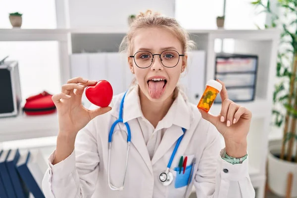 若いですCaucasian医師女性保持丸薬と心臓スティック舌アウト幸せとともに面白い式 — ストック写真