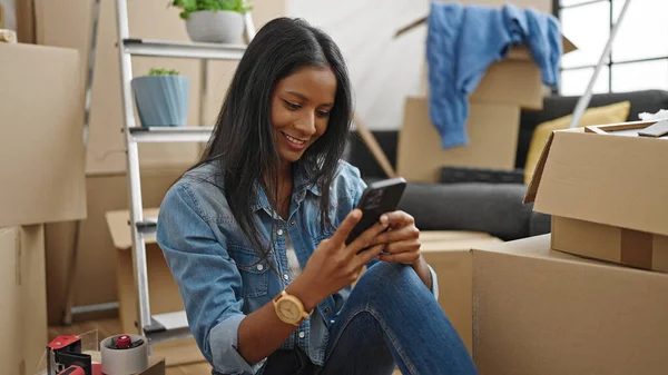 使用智能手机的非洲裔美国妇女坐在新家的地板上 — 图库照片