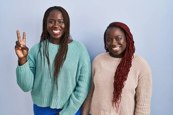 Две Африканки Стоят Синем Фоне Показывают Пальцем Номер Два Улыбаясь — стоковое фото