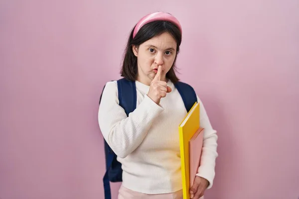 ダウン症候群の学生のバックパックを着て 本を唇に指で静かにするように求めて保持している女性 沈黙と秘密の概念 — ストック写真