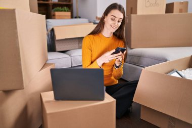 Young caucasian woman using laptop and smartphone at new home