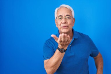 Mavi arka planda gri saçlı, orta yaşlı bir adam kameraya bakıp havada bir öpücük savuruyor ve güzel ve seksi oluyor. aşk ifadesi. 