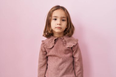 Yüzünde ciddi bir ifadeyle pembe arka planda duran küçük İspanyol kız. Basit ve doğal bir şekilde kameraya bakıyorsun.. 