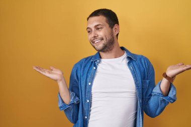 Sarı arka planda duran İspanyol adam gülümsüyor. İki elini de açık tutuyor. Karşılaştırma ve reklam karşılaştırması yapıyor ve dengeyi sağlıyor. 