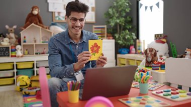 Young hispanic man preschool teacher having online vocabulary lesson at kindergarten