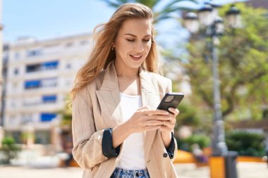 Parkta akıllı telefon kullanan, kendine güvenen genç sarışın kadın.