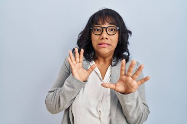 Hispanic woman standing over isolated background afraid and terrified with fear expression stop gesture with hands, shouting in shock. panic concept. 