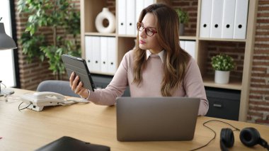 Young beautiful hispanic woman business worker using touchpad and laptop at office