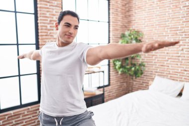 Genç İspanyol adam gülümseyerek yatak odasında kendine güvenen yoga eğitimi alıyor.