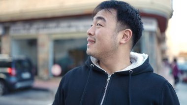 Young chinese man smiling confident looking to the side at street