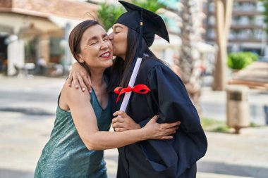 Two women mother and graduated daughter holding diploma kissing at street