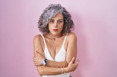 Pembe arka planda duran gri saçlı orta yaşlı kadın yüzünde üzgün bir ifadeyle kış soğuğundan titriyor ve donuyor. 