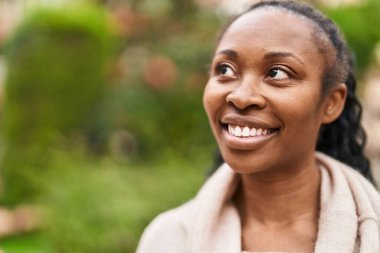 Afro-Amerikalı kadın parkta kendinden emin bir şekilde gülümsüyor.