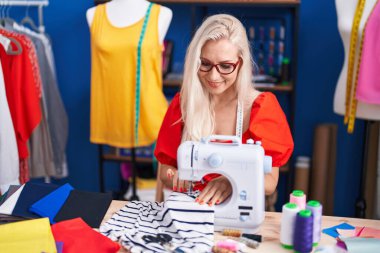 Dikiş atölyesinde dikiş makinesi kullanan kendine güvenen genç sarışın kadın terzi.