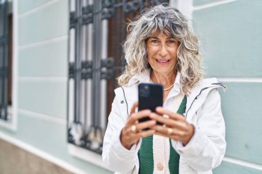 Sokakta akıllı telefon kullanan orta yaşlı bir kadın gülümsüyor.