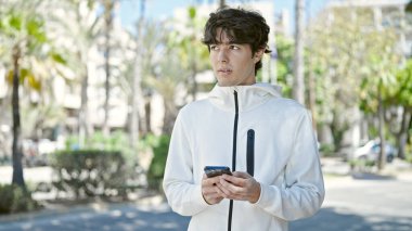 Genç İspanyol bir adam parkta akıllı telefon kullanıyor.