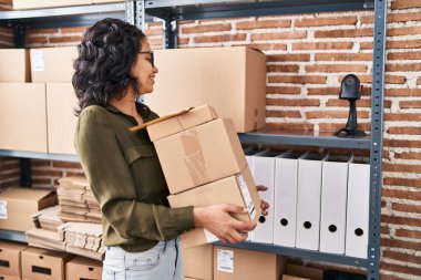 Genç Latin kadın ecommerce iş işçisi ofiste paketler tutuyor.