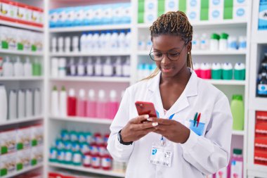 Eczanede çalışan akıllı telefonu kullanan Afrikalı Amerikalı kadın eczacı.