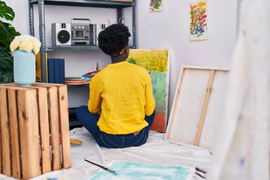 Young african american woman artist drawing sitting on floor at art studio