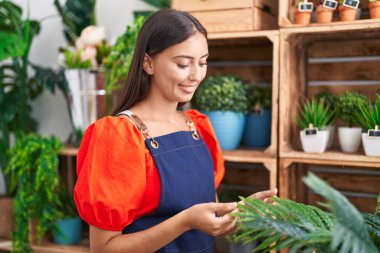 Young beautiful hispanic woman florist smiling confident touching sheet plant at florist