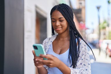 Afro-Amerikalı kadın sokakta akıllı telefon kullanarak kendine güveniyor.