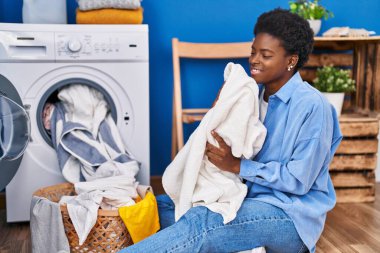 African american woman smelling towel using washing machine at laundry room