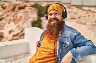 Young redhead man smiling confident listening to music at street