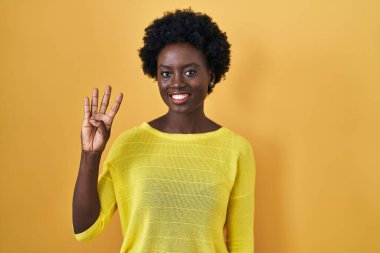 Sarı stüdyonun başında duran Afrikalı genç bir kadın kendini beğenmiş ve mutlu bir şekilde gülümserken dört numarayı gösterip işaret ediyor.. 