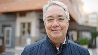 Orta yaşlı, gri saçlı, kendine güveni olan bir adam.