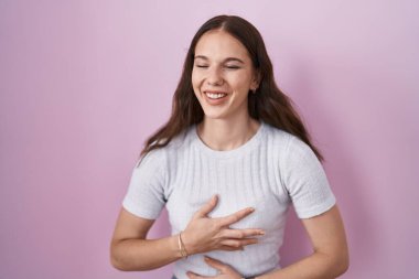 Pembe arka planda duran genç İspanyol kız gülümseyerek ve kahkahalarla gülüyor çünkü elleri vücutta olan komik çılgın bir şaka.. 