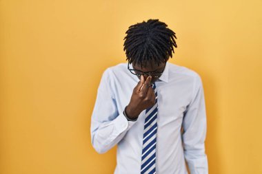 Sarı arka planda duran Afrikalı adam yorgun burnu ve gözleri ovuşturup yorgun ve baş ağrısı çekiyor. Stres ve hüsran kavramı. 