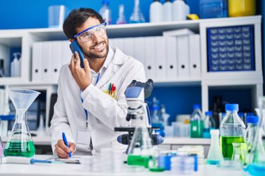 Genç İspanyol bilim adamı akıllı telefondan konuşuyor. Laboratuvarda yazılı belge var.