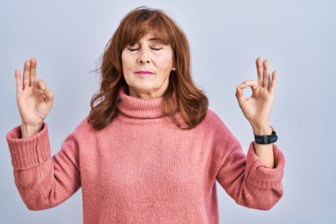 Orta yaşlı İspanyol bir kadın izole edilmiş arka planda durup rahatlamış ve parmaklarıyla meditasyon hareketi yaparken gözleri kapalı gülümsüyor. yoga konsepti. 